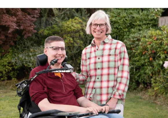 A young man using a powered wheelchair with a family member outdoors